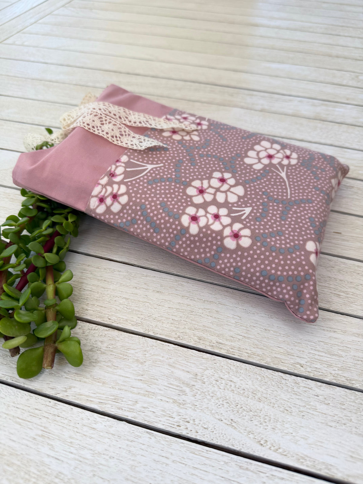 Side view of a handmade dusty pink fabric book sleeve lying horizontally on a wooden surface, showing its floral pattern, shape and thickness.