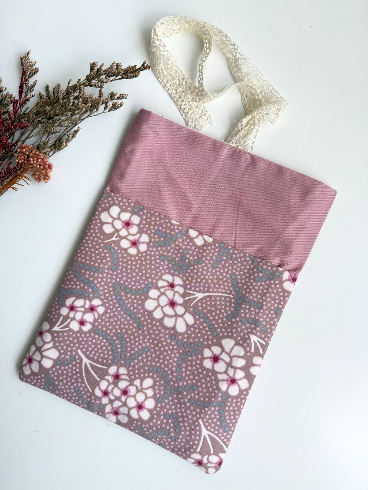 Empty handmade dusty pink fabric book sleeve laid flat, showing the floral front pocket and cream lace ribbon closure without a book inside.