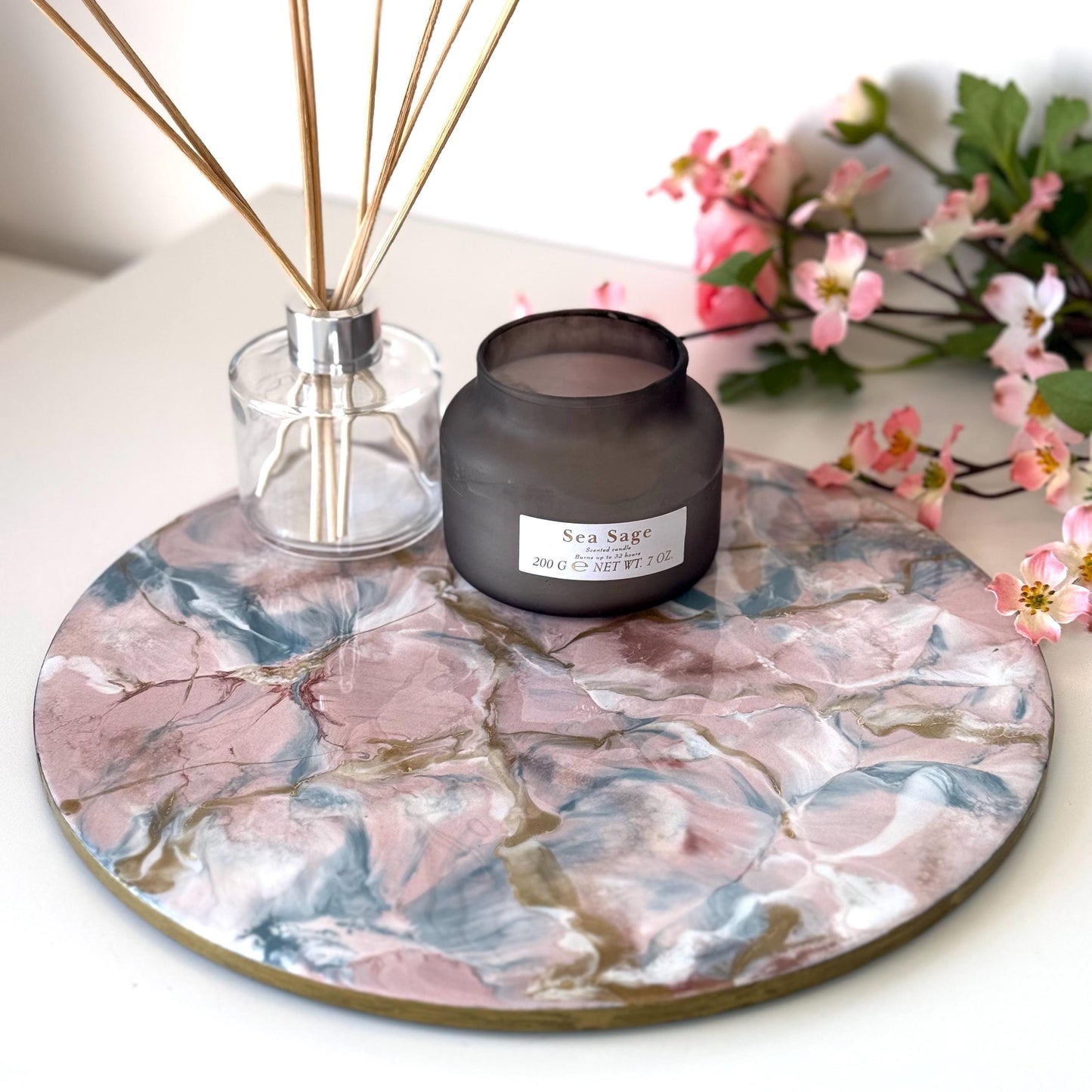 Pink and gold marble-style resin tray with slate base, round centrepiece styled with candles and diffuser, flowers in the background, handmade decorative tray for home display or serving.