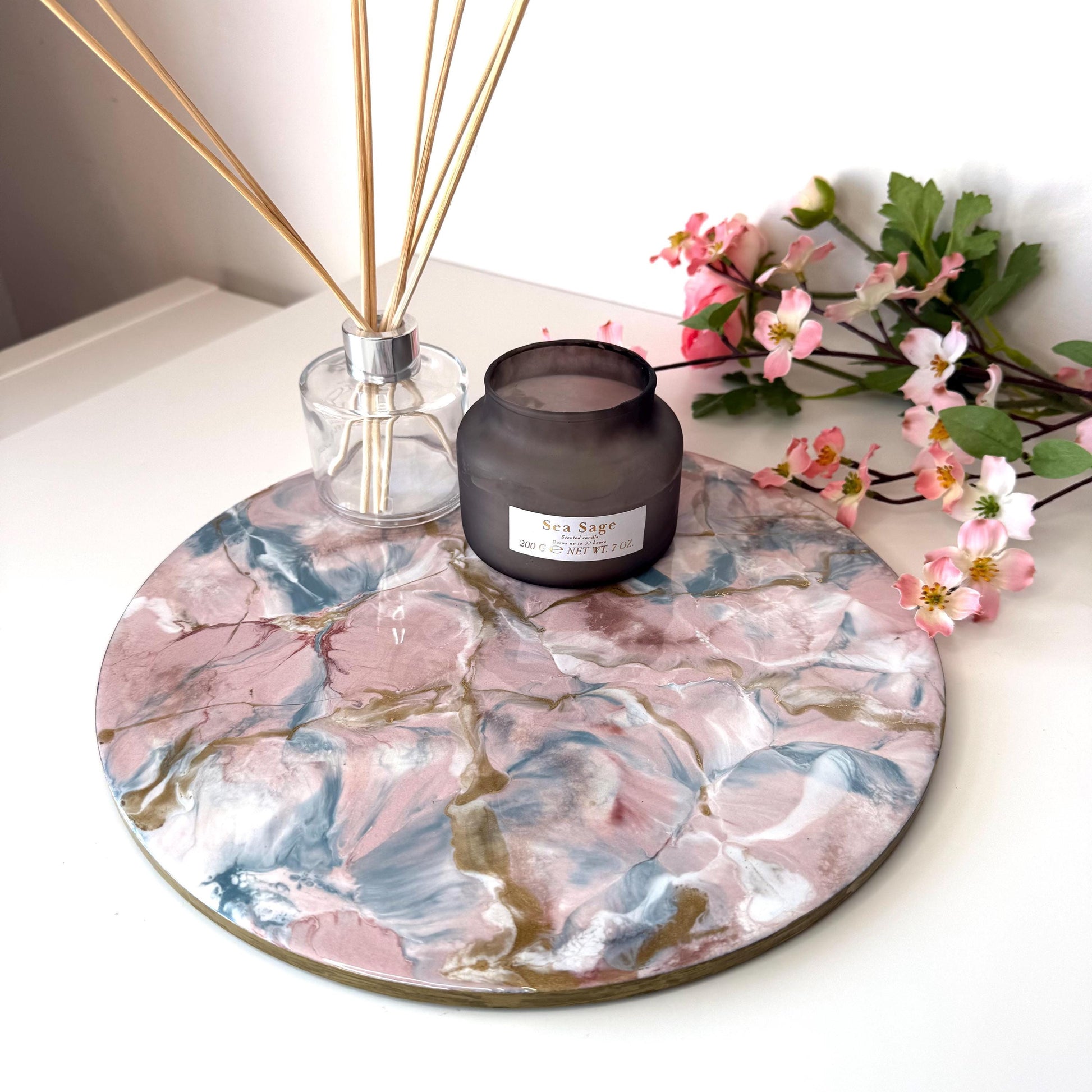 Pink and gold marble-style resin tray with slate base, round centrepiece styled with candles and diffuser, flowers in the background, elegant handmade decorative tray for home display or serving