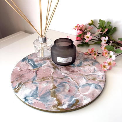 Pink and gold marble-style resin tray with slate base, round centrepiece styled with candles and diffuser, flowers in the background, elegant handmade decorative tray for home display or serving