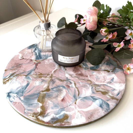 Pink and gold marble-style resin tray with slate base, round centrepiece, styled with candles and diffuser, flowers in the background, handmade decorative tray for home display or serving.