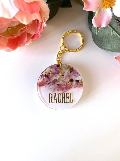 Pink and white round resin keychain with dried flowers and gold leaf, personalised in uppercase capital gold vinyl font, handmade resin keyring for gifts