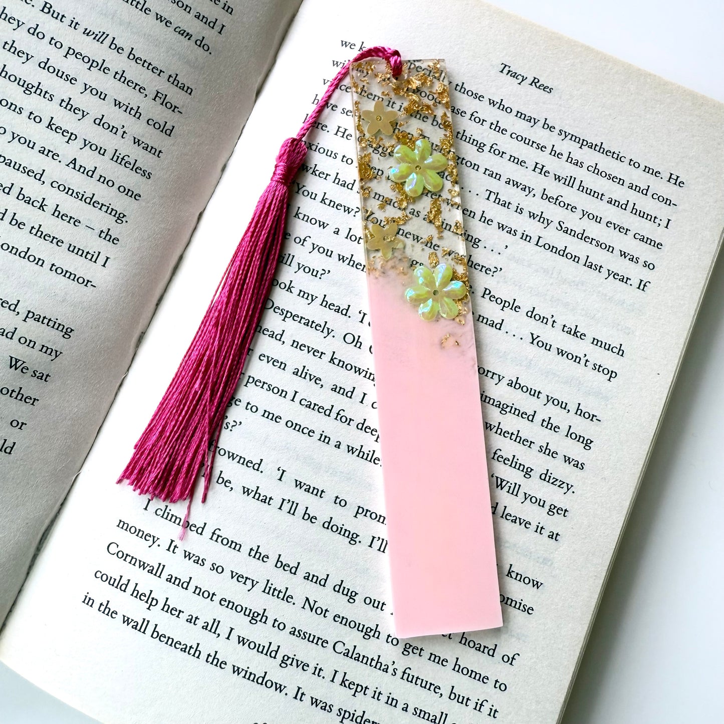 Plain pink resin bookmark with floral design on an open book, featuring a matching tassel.