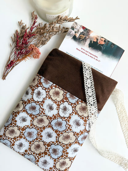 Brown faux suede paperback book sleeve with vintage floral cotton front pocket, cream lace ribbon and a paperback book protruding from the top.
