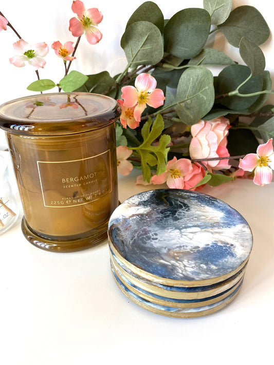 Stack of round slate resin coasters with blue, white, black, and gold epoxy design and gold-painted edges, styled on a coffee table – elegant handmade home décor.