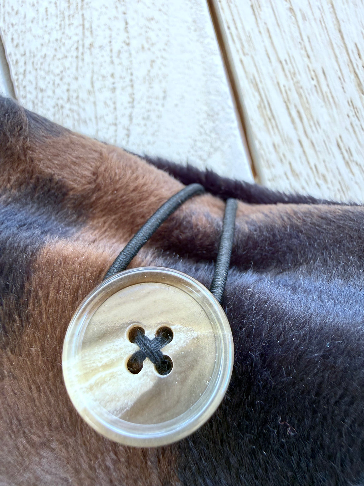 Close-up of the round pearlescent button and black elastic loop closure on a handmade black and brown velvet book sleeve.