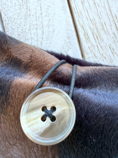 Close-up of the round pearlescent button and black elastic loop closure on a handmade black and brown velvet book sleeve.